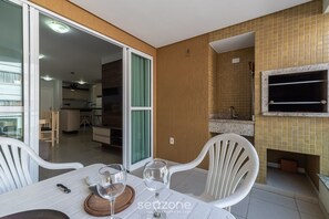 Zona pranzo con tavolo apparecchiato per due, cucina sullo sfondo e camino con TV a parete.