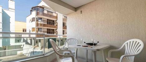 Un balcon avec deux chaises en plastique blanches et une petite table, donnant sur un paysage urbain avec des bâtiments modernes.