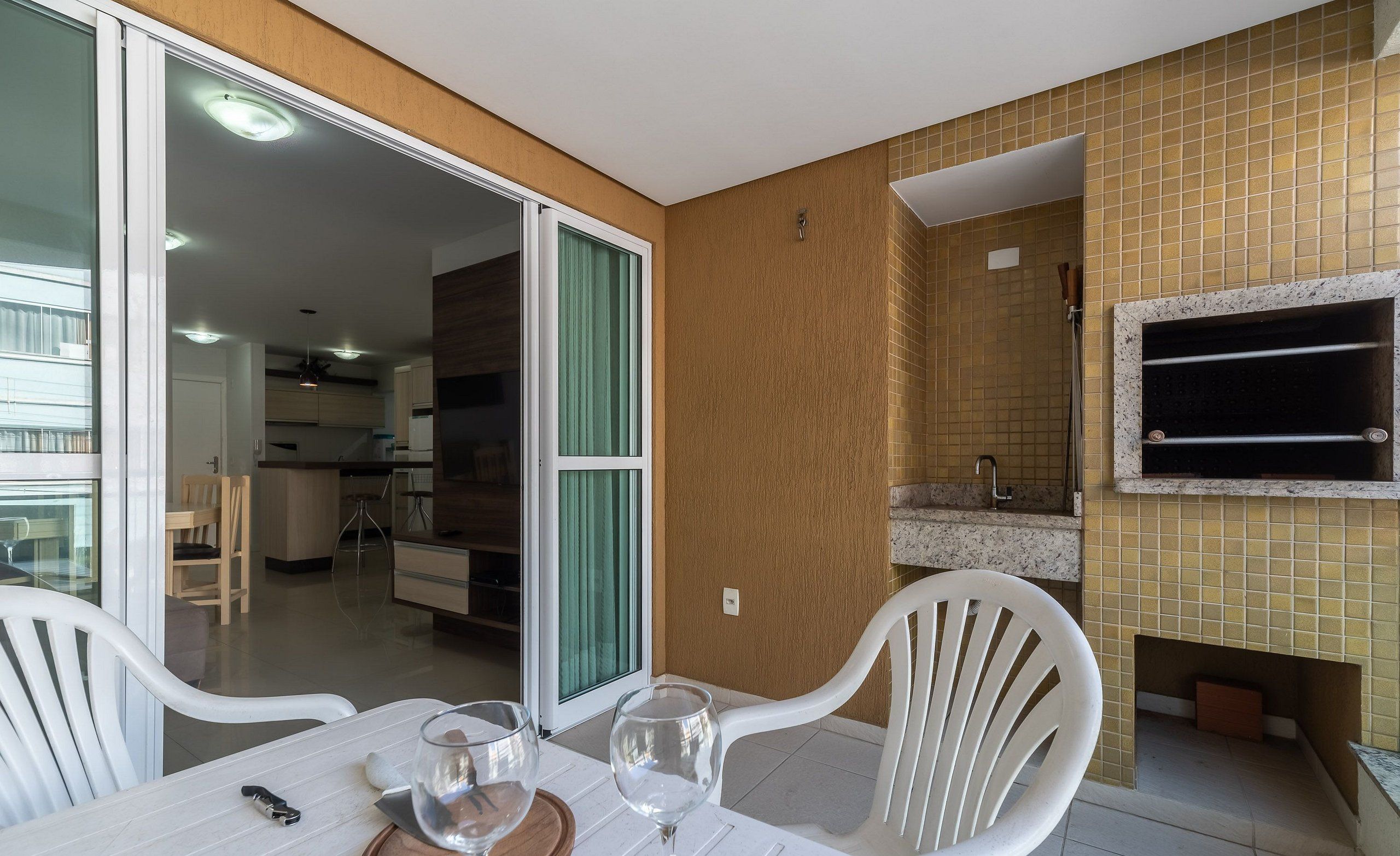A dining area with a table set for two, a kitchen in the background, and a fireplace with a TV mounted on the wall.