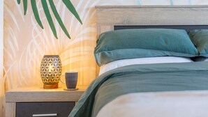 A neatly made bed with green bedding, a bedside table with a patterned lamp, and a cup.