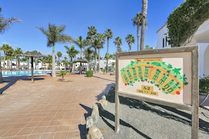 A tiled patio area with palm trees, a pool, and a signboard with information.