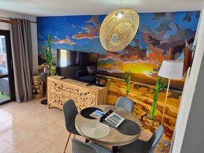 Un soggiorno con televisione, un mobile in legno, un tavolo rotondo con sedie, un affresco e una lampada a sospensione.