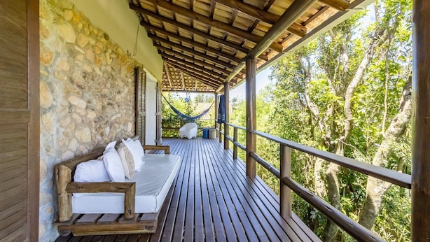 A wooden deck with a stone wall, a hammock, and a white sofa with pillows. - Comfortable Duplex in Praia do Rosa - SC Rfe000 (Imbituba)