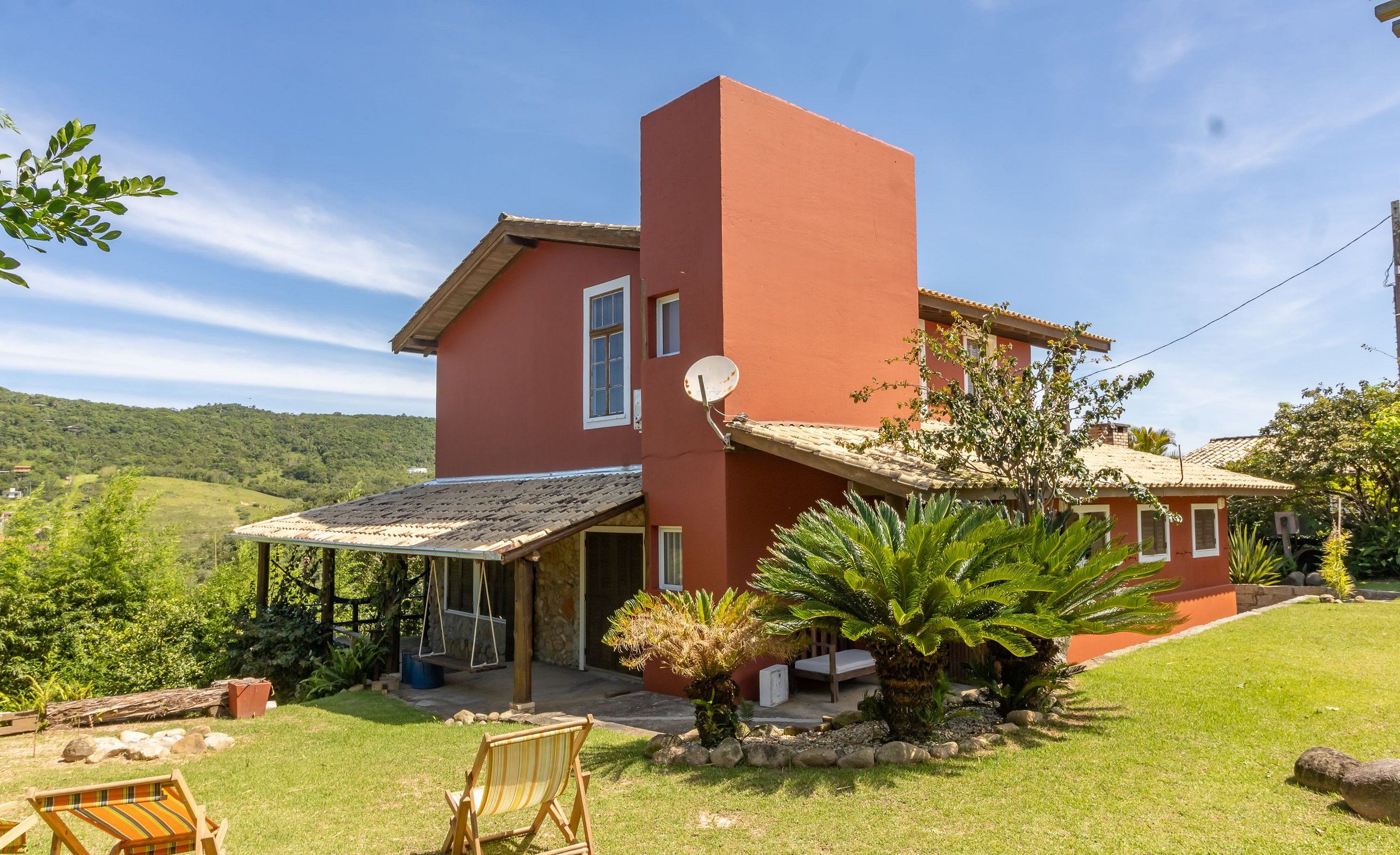 Una casa roja con un porche cubierto, una antena parabólica y un patio césped con una palmera.