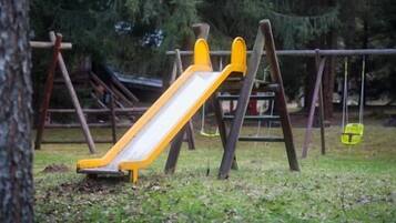 Un'area giochi con uno scivolo giallo e altalene, immersa nel verde.