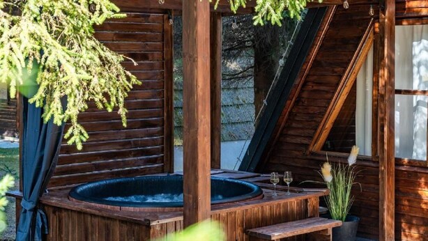 Un jacuzzi de madera con escalones que llevan a él, rodeado por una terraza de madera y una puerta de cristal.