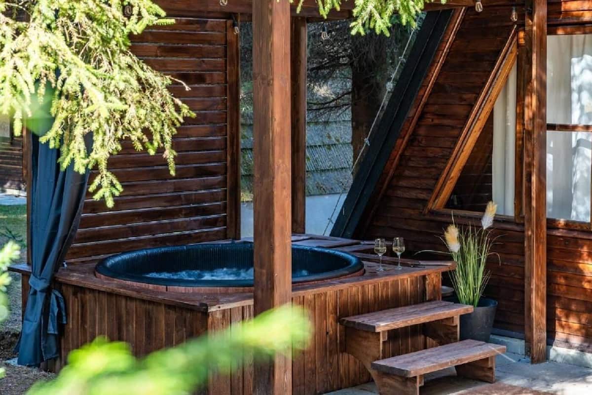 A wooden hot tub with steps leading up to it, surrounded by a wooden deck and a glass door.