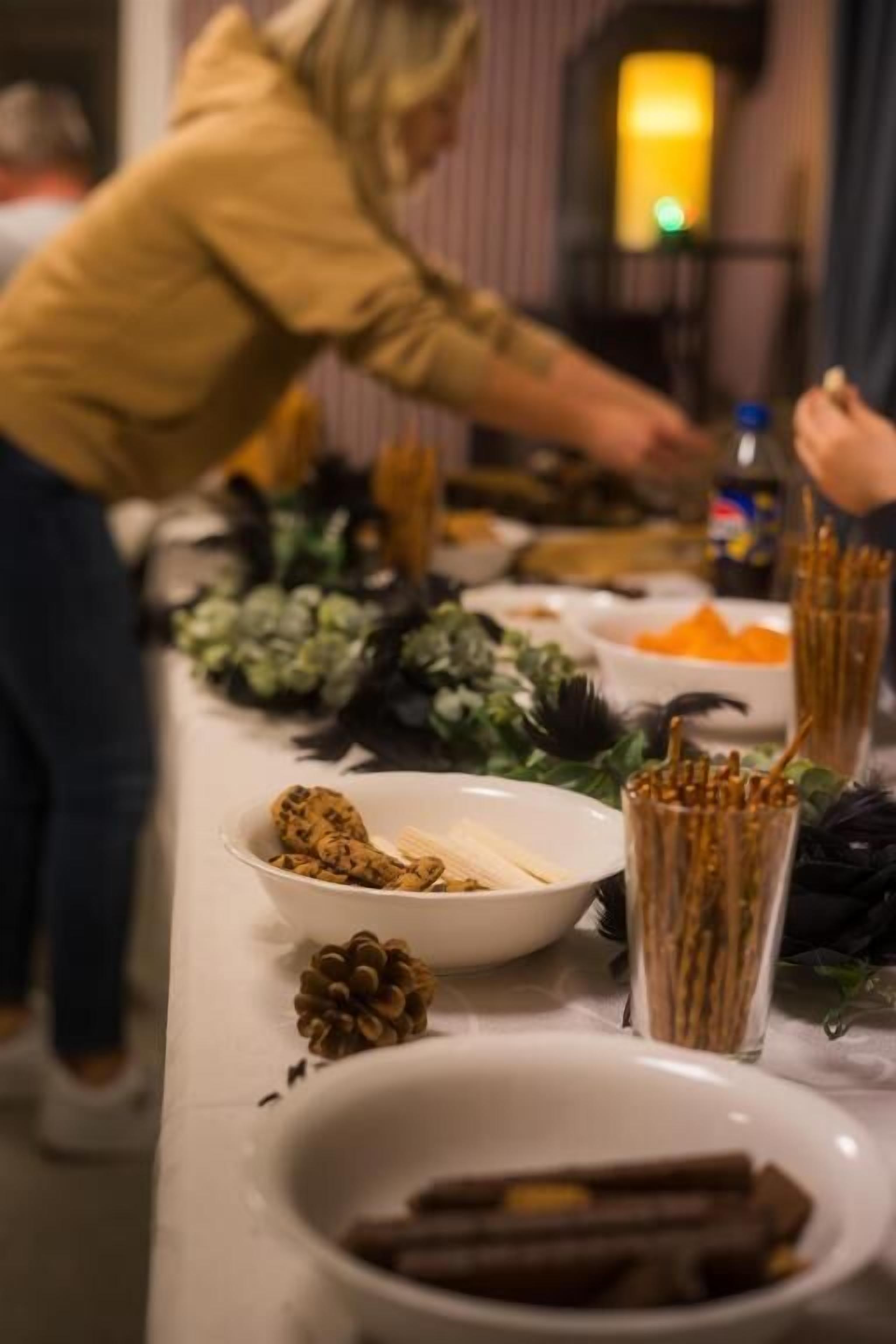 A table with various food items and decorations, including a bowl of cookies, a pine cone, and a glass with sticks.