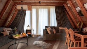 Habitación en el ático con techo de madera, un sofá, una mesa de comedor y una chimenea.