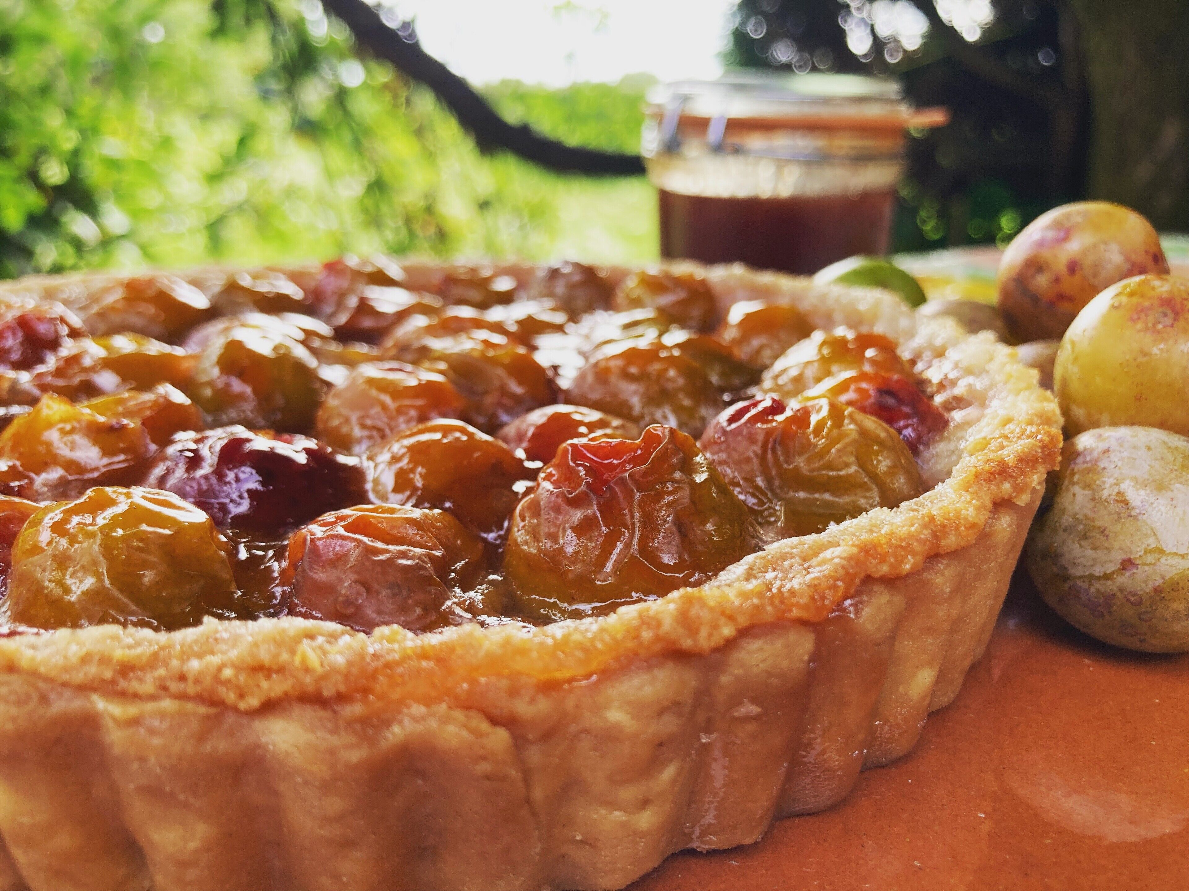 Piirakka, jonka reunat ovat rapeat, täytteenä marjoja tai hedelmiä, ja taustalla näkyy purkki.