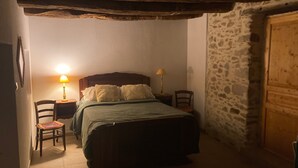 Ein Schlafzimmer mit einem Bett, zwei Nachttischen mit Lampen, einem Sessel und einer Steinwand.