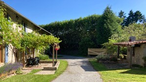 Ein Kiesweg führt zu einem rustikalen Gebäude mit einer Pergola und hängenden Blumenkörben.