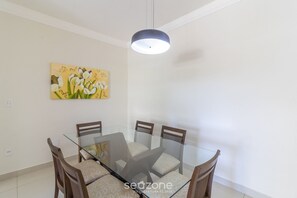 Egy étkezősarok üveglappal ellátott asztallal és fa székekkel, egy kép a falon, és egy mennyezeti lámpatest.
