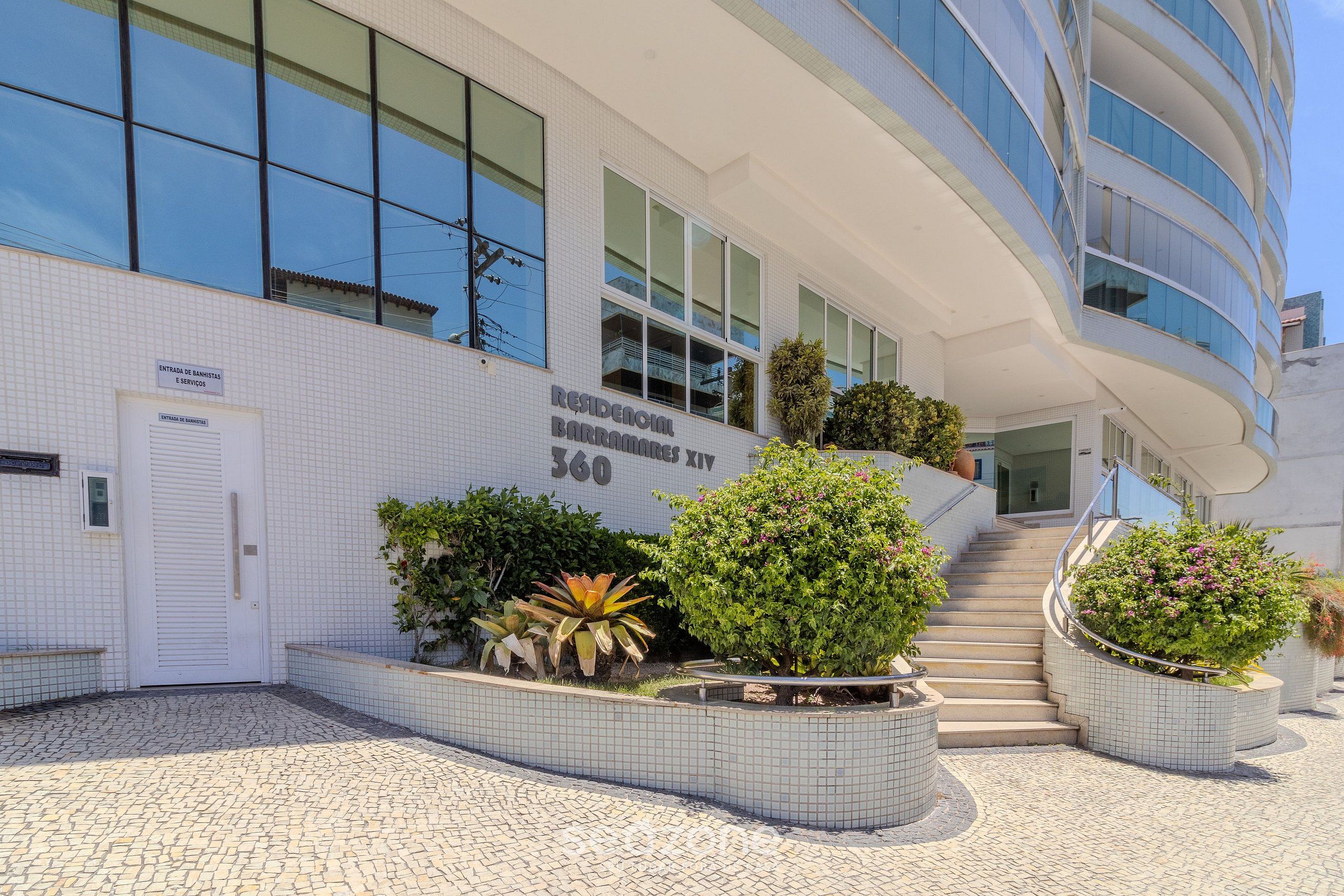 A modern building with a tiled facade, a staircase leading to the entrance, and landscaped planters.