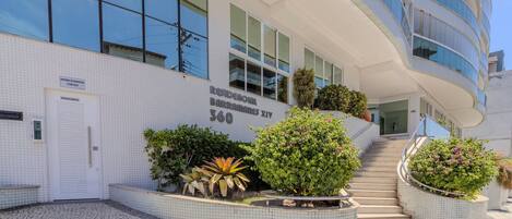A modern building with a tiled facade, a staircase leading to the entrance, and landscaped planters.