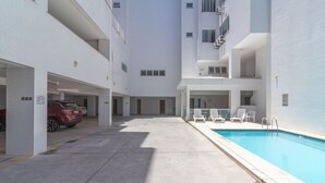 En modern byggnad med en swimmingpool, flera balkonger och en parkeringsplats med en röd bil.