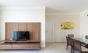 Uma sala moderna com televisão de tela plana em um móvel de madeira, uma mesa de jantar com cadeiras e uma porta que dá para outro cômodo.