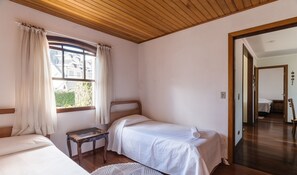 Ένα υπνοδωμάτιο με δύο μονά κρεβάτια, ένα μικρό τραπέζι και ένα παράθυρο με κουρτίνες.