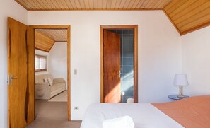 Une chambre à coucher comprenant un lit, une table de chevet, une lampe et donnant sur un espace de vie avec un canapé et une fenêtre.