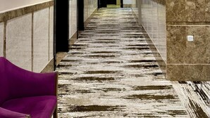 Un corridoio d'albergo con una moquette a fantasia, pareti in marmo e una poltrona viola.