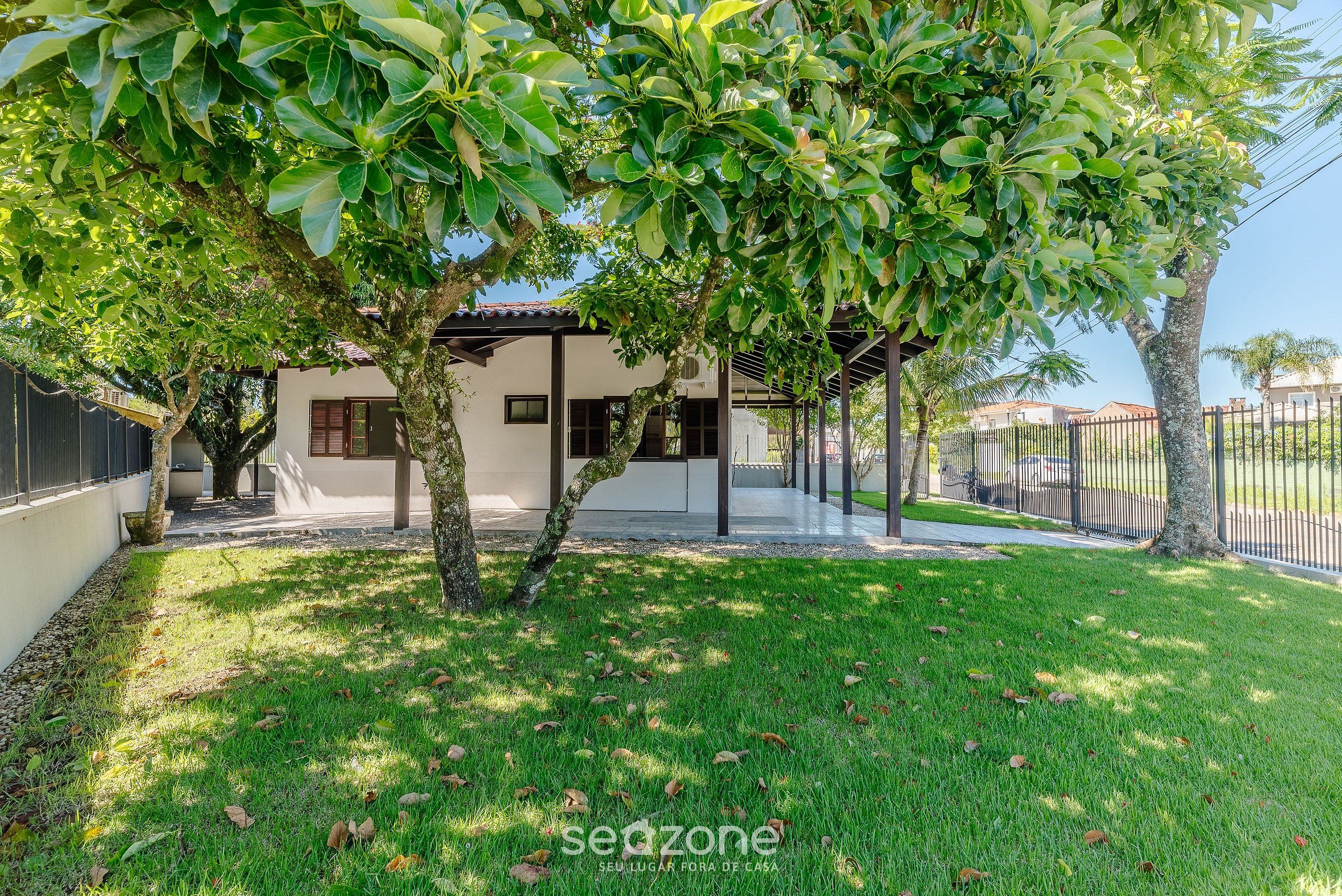Una casa moderna amb un porxo cobert, un jardí ben cuidat i un arbre al primer pla.