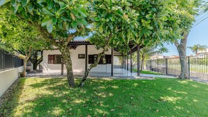 A modern house with a covered patio, a well-maintained lawn, and a tree in the foreground. - 3BR Home w/ BBQ 140m From the Beach Rae0126 (Bombinhas)