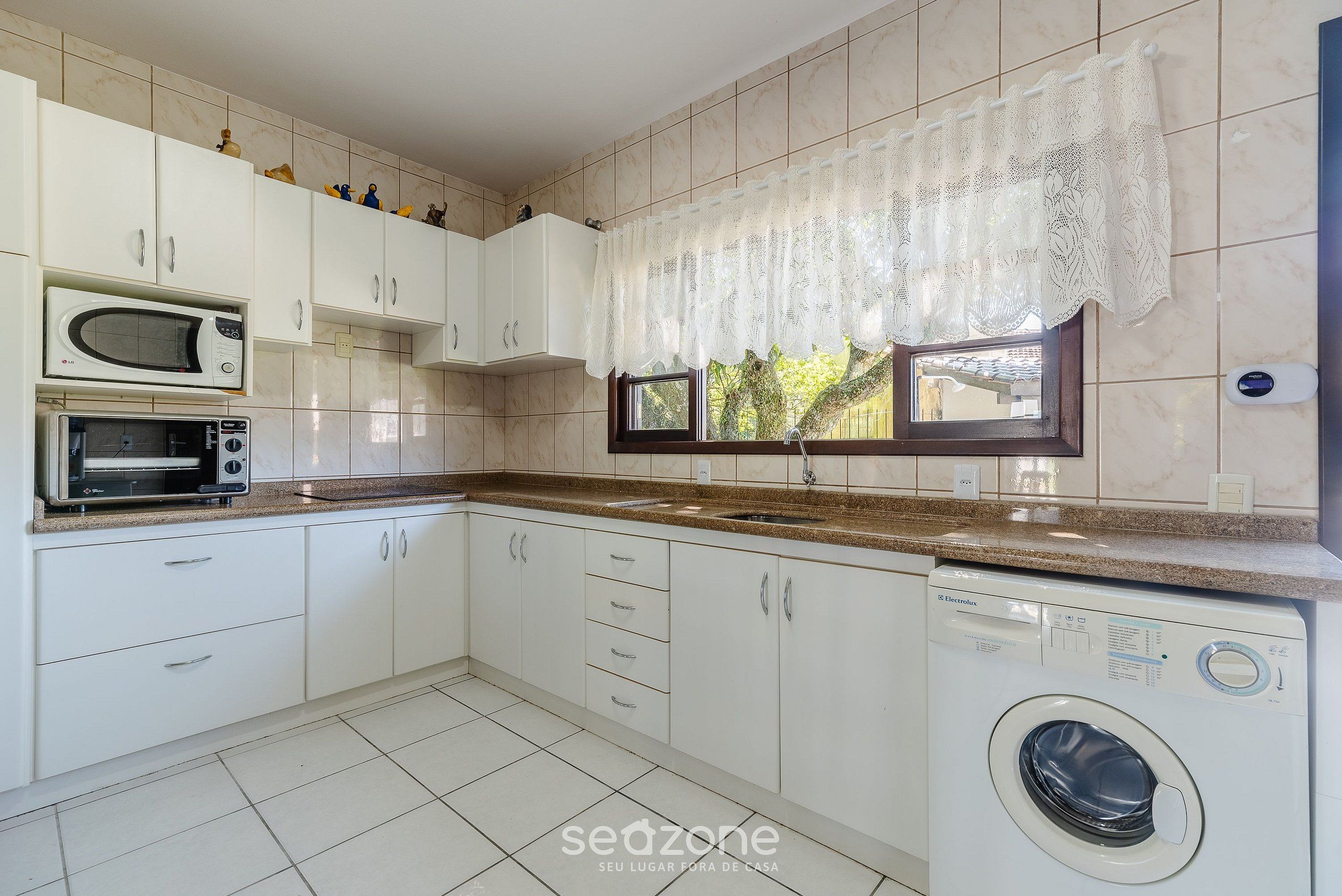 A kitchen with white cabinets, a microwave, a toaster, a sink, and a washing machine.