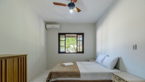 A bedroom with a bed, a wooden cabinet, a nightstand, a ceiling fan, and a window with a view of greenery. - 3BR Home w/ BBQ 140m From the Beach Rae0126 (Bombinhas)
