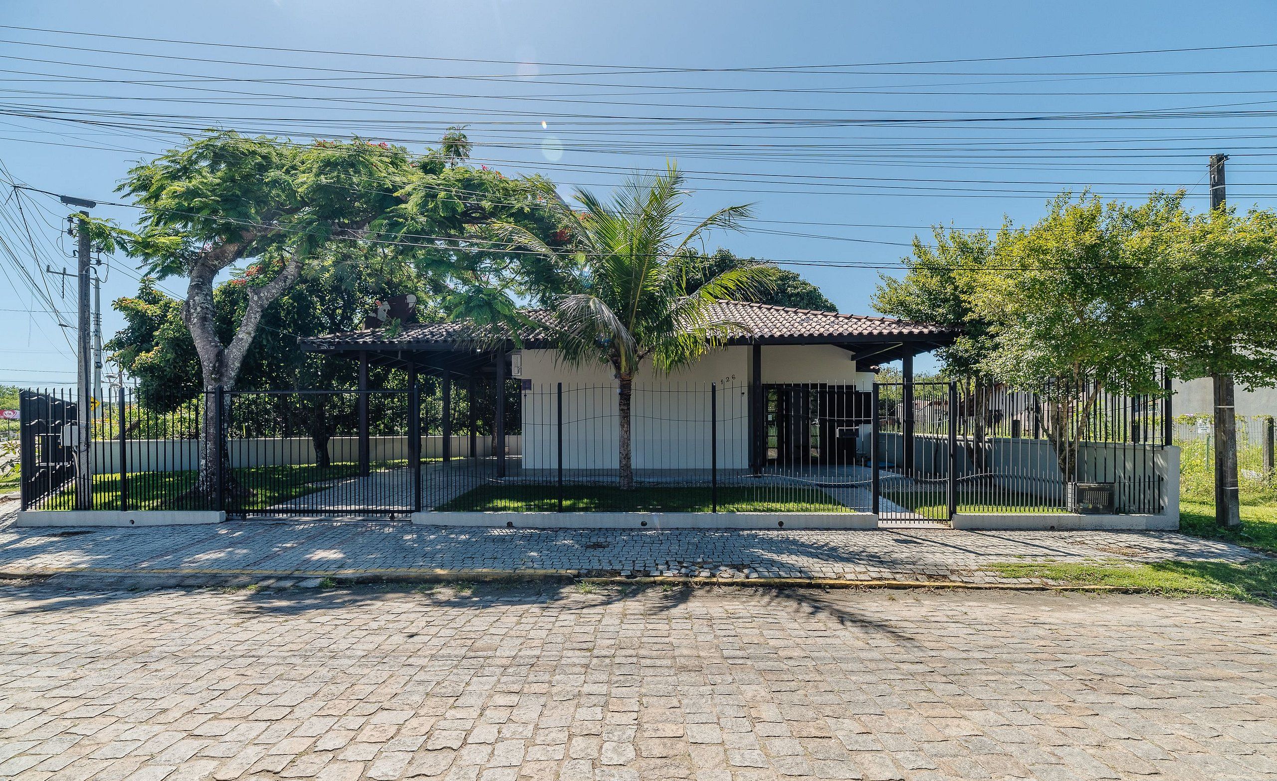 A paved driveway leading to a gated property with a covered patio, surrounded by trees and a fence.