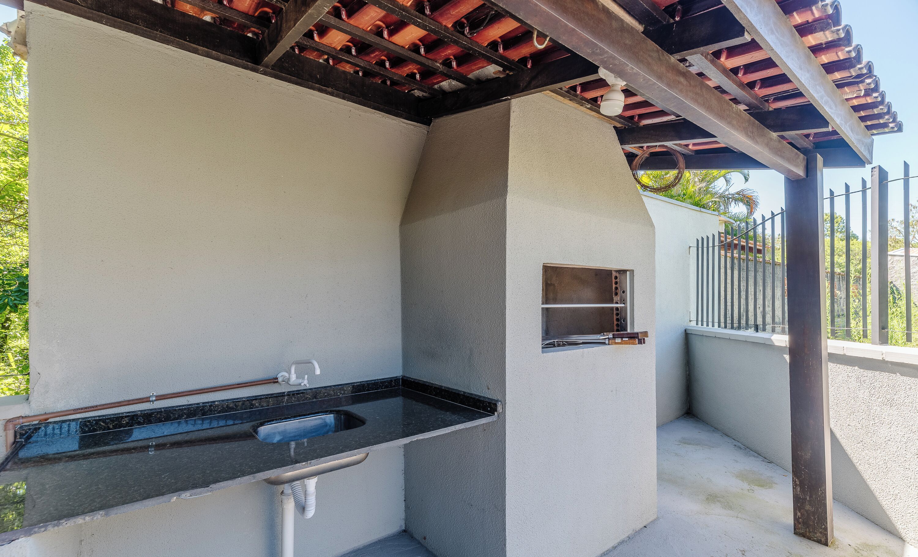 Un área de cocina al aire libre con pileta integrada, parrilla y una estructura de pérgola.