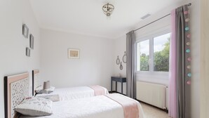 Un dormitori amb dos llits, una finestra amb cortines, un radiador i decoració penjada a la paret.
