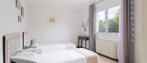 A bedroom with two beds, a window with curtains, a radiator, and wall-mounted decor.
