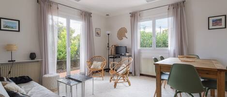 A room with a sofa, two wicker chairs, a dining table with chairs, a ceiling fan, and a TV.
