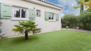 Una casa de façana blanca, persianes verdes i un jardí ben cuidat.