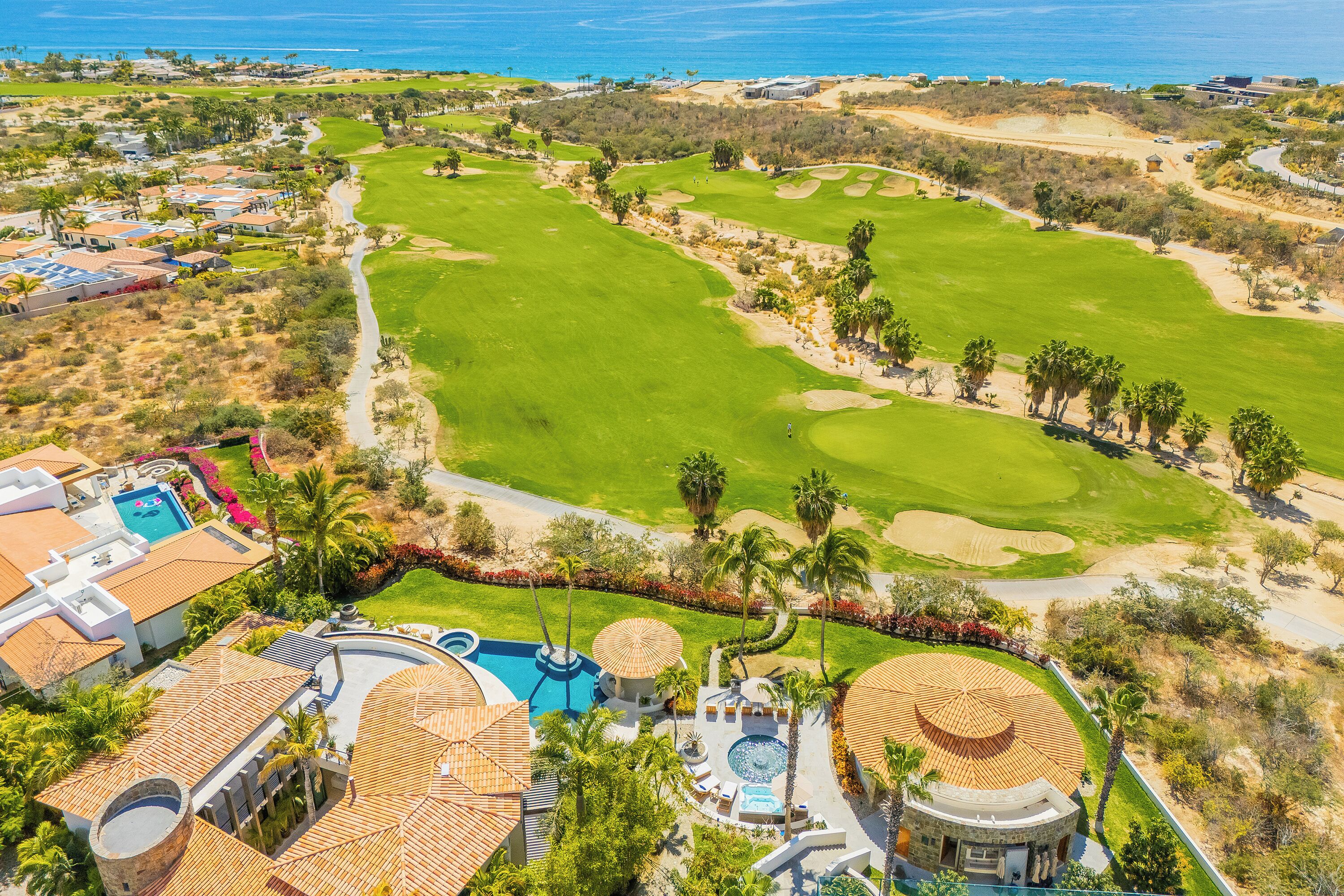 A golf course with a swimming pool, palm trees, and a view of the ocean.