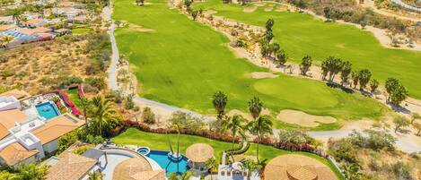 A golf course with a swimming pool, palm trees, and a view of the ocean.