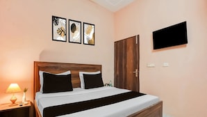 A neatly arranged bedroom with a wooden bed frame, a bedside table with a lamp, and a flat-screen TV mounted on the wall. - Hotel O Green City Dhakoli Formerly Swagat (Dera Bassi)