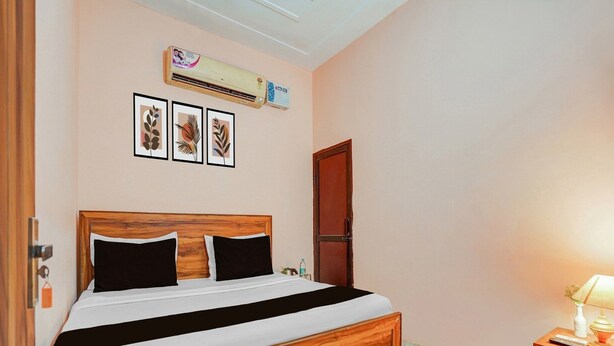 A bedroom with a wooden bed, a wall-mounted air conditioner, and framed artwork. - Hotel O Green City Dhakoli Formerly Swagat (Dera Bassi)