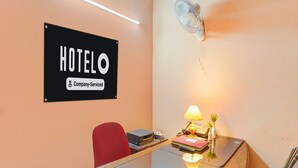 A hotel room with a desk, a red chair, a wall-mounted fan, a lamp, and a sign that reads 'HOTELO Company Serviced'. - Hotel O Green City Dhakoli Formerly Swagat (Dera Bassi)