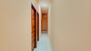 A narrow hallway with wooden doors on one side and a tiled floor. - Hotel O Green City Dhakoli Formerly Swagat (Dera Bassi)