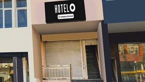 A hotel entrance with a closed shutter, steps leading up to the entrance, and a sign indicating it is company-serviced. - Hotel O Green City Dhakoli Formerly Swagat (Dera Bassi)