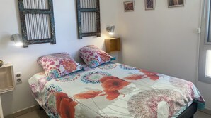 A bedroom with a floral bedspread, two wall-mounted light fixtures, and two framed pictures on the wall.