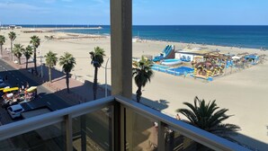 A beach view from a balcony with palm trees, a sandy beach, and a water slide.