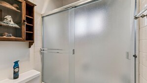 Un baño con cabina de ducha de vidrio, inodoro blanco y un mueble con objetos decorativos.
