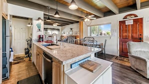 A spacious kitchen with a large island, wooden ceiling beams, pendant lighting, and a view of the outdoors. - 439AW Tahoe Keys Studio Perfect Couples Get Away (South Lake Tahoe)