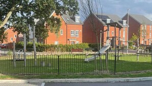 A playground with a slide and a fenced area, surrounded by a brick building with multiple windows.