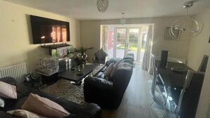 A living room with a sofa, a coffee table, a TV, and a dining area with a table and chairs.
