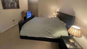 A bedroom with a bed, a television on a stand, a lamp, and a painting on the wall.