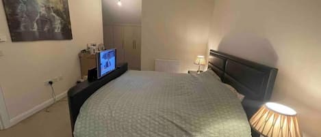 A bedroom with a bed, a television on a stand, a lamp, and a painting on the wall.