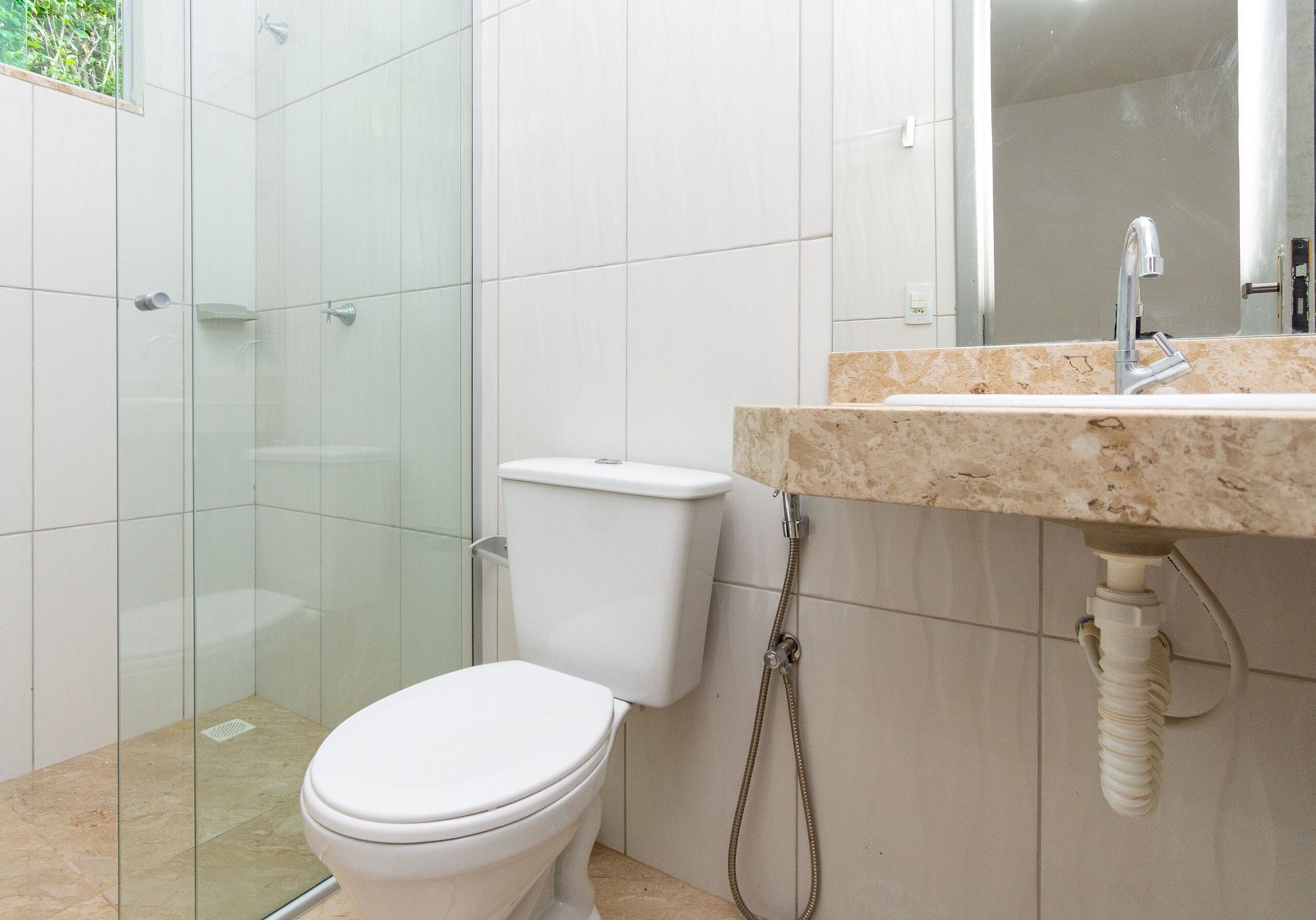 Ein Badezimmer mit Duschkabine aus Glas, einer weißen Toilette und einem Waschbecken mit Marmorplatte.